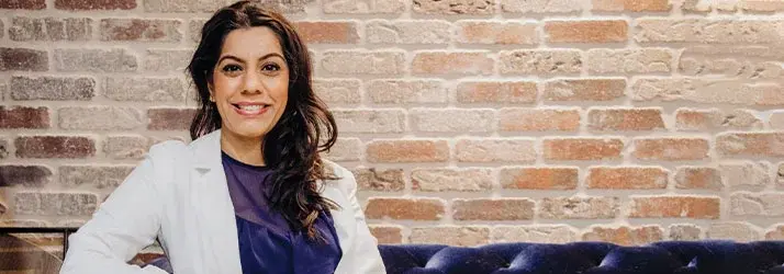 Smiling woman seated in front of a brick wall.