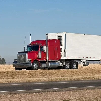 Red semi-truck with a white trailer beside a rural road.